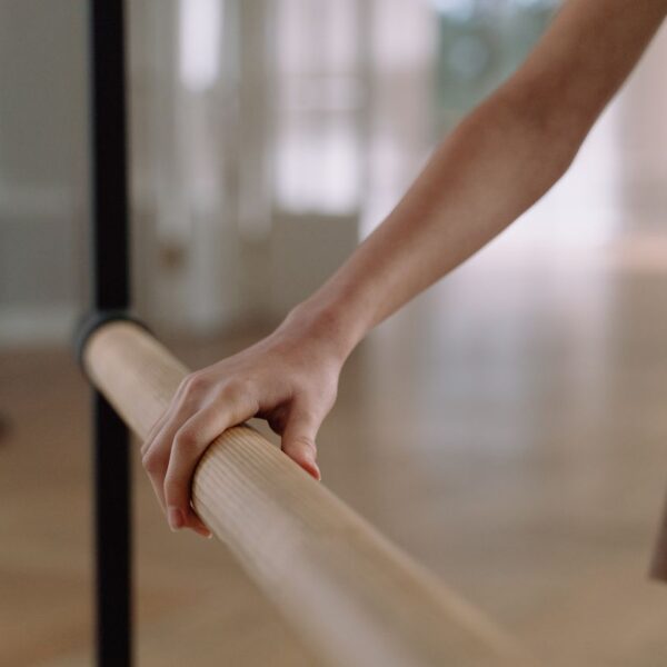 Close-up of a ballet dancer's hand holding a wooden barre in a dance studio.